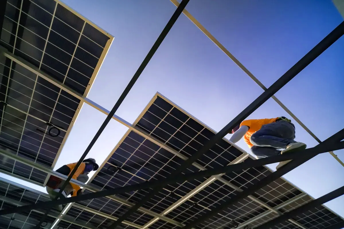 Estructura de paneles solares vista desde abajo con técnicos trabajando, como en los proyectos de PHPT en Hospitalet